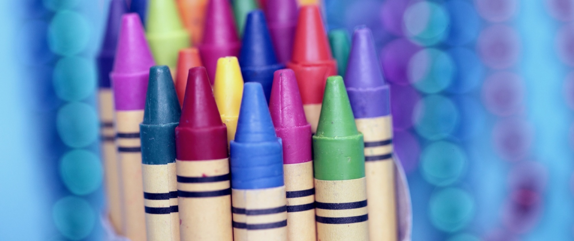 Close-up shot of multi-coloured crayons against an out-of-focus purple and blue background