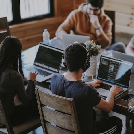 Image of people sitting at a shared workstation each working on individual laptops