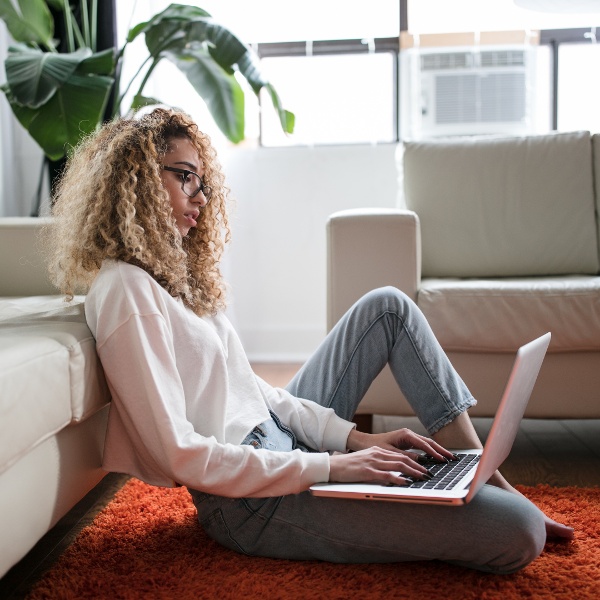 Side profile image of a female-presenting person sitting on the floor while working on their laptop